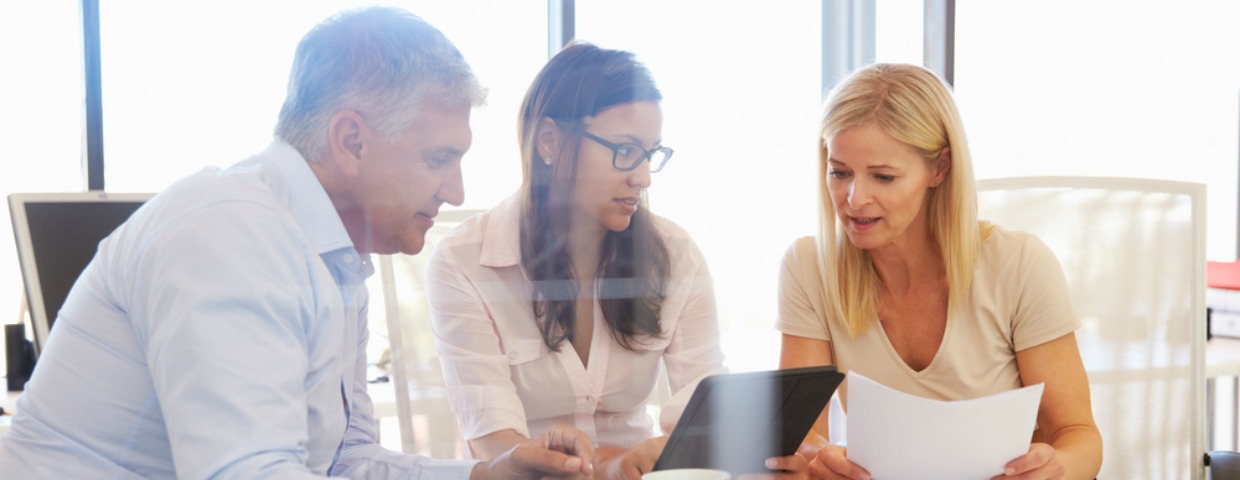 Three workers sitting around a desk looking at documents