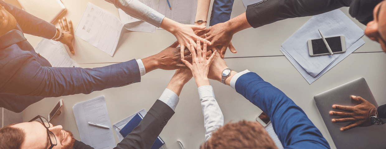 Group of business people in a circle extending their hands to have them all meet in the middle