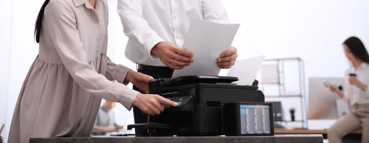 Two people standing by and working on a multifunction printer