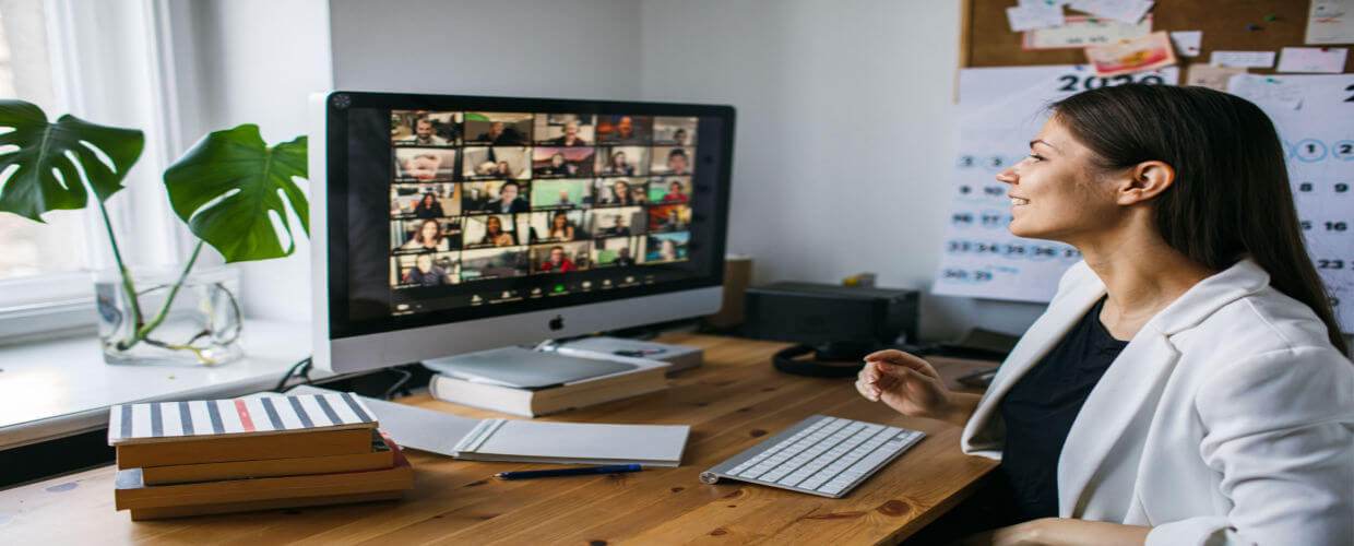 Woman at desk smiling having a video conference call with many people
