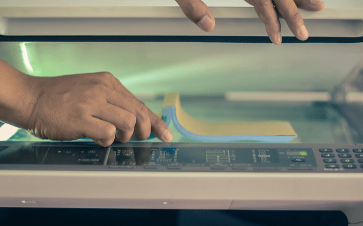 Pair of hands lifting the lid of a scanner and placing a document on it for scanning