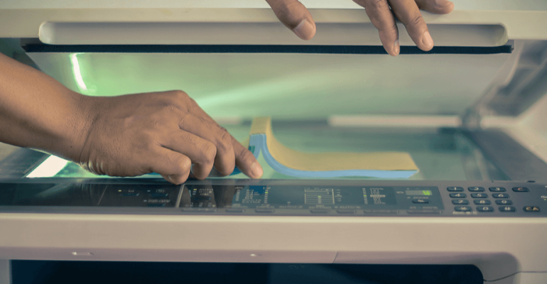 Pair of hands lifting the lid of a scanner and placing a document on it for scanning