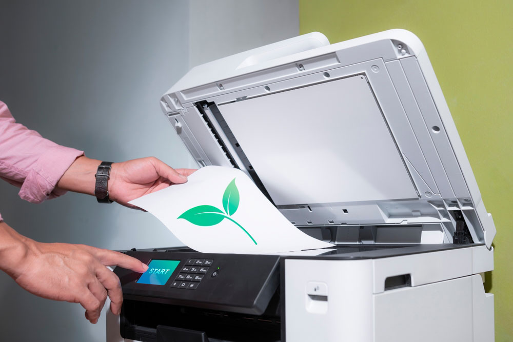 Multifunction printer with lid open person copying a document with a green leaf on it